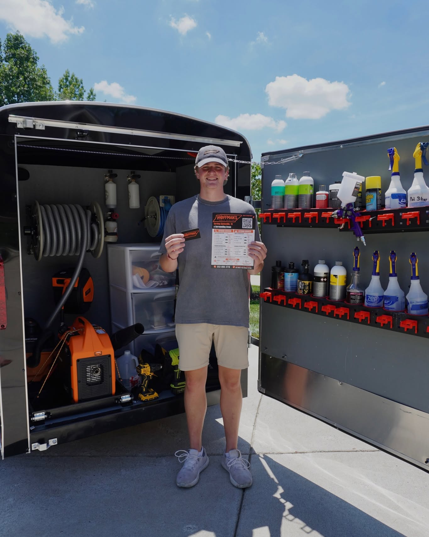 Sam Hoffman standing inside his open detailing trailer — showing the organized interior with a pressure washer, chemical rack, and professional-grade supplies